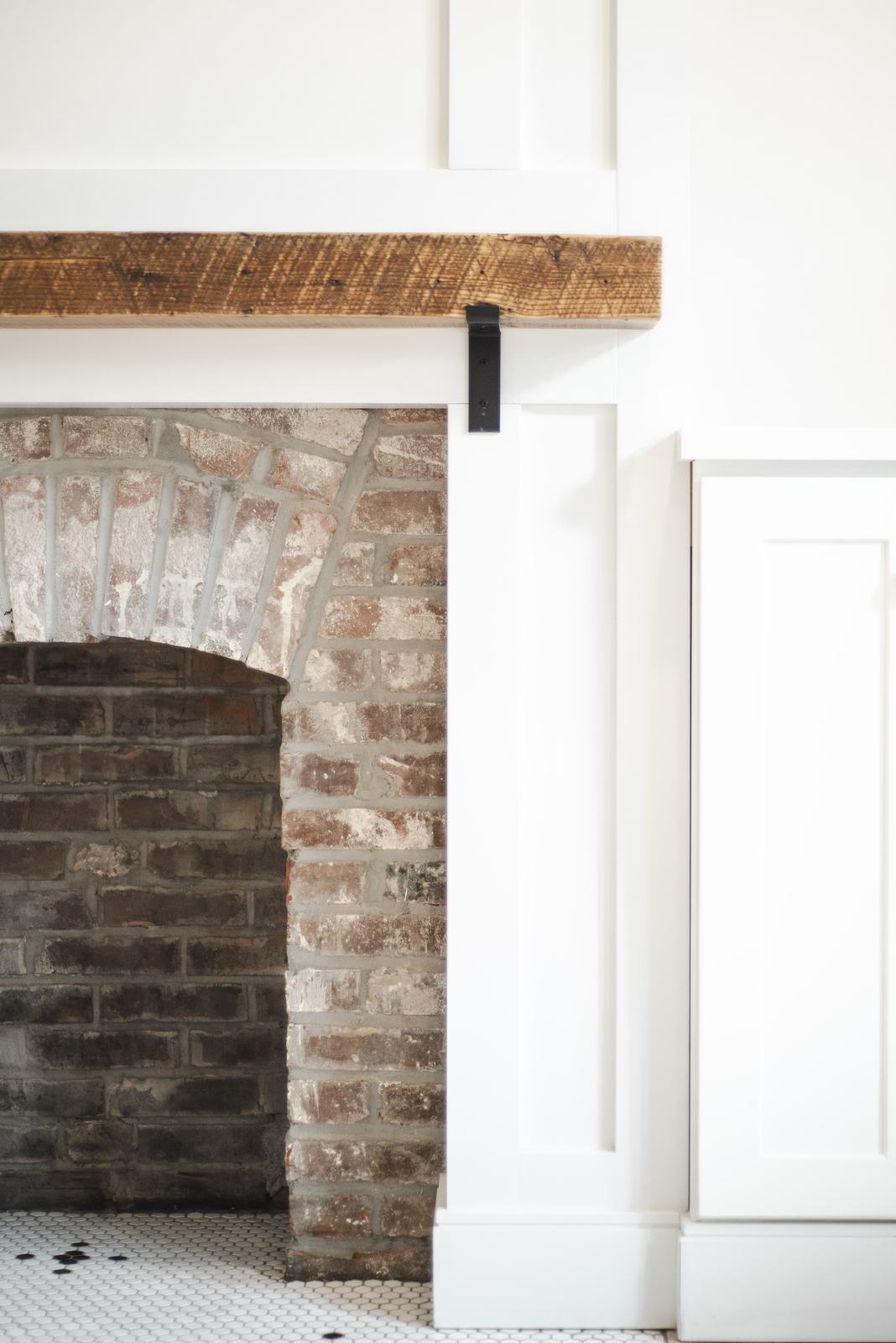 Whitewashed brick fireplace with a reclaimed wood mantel